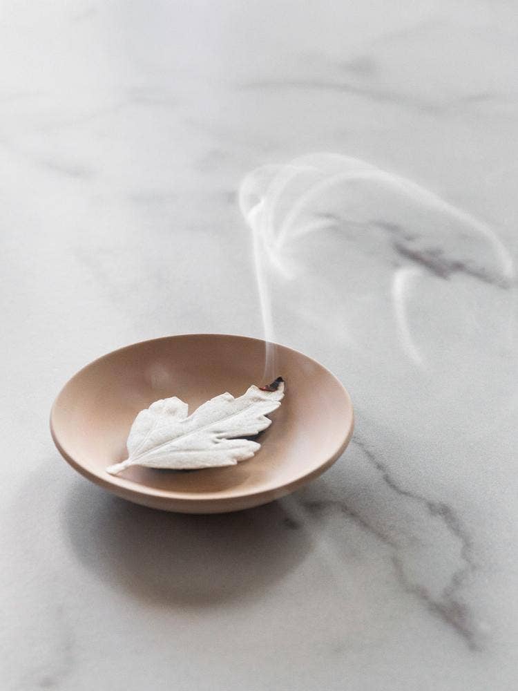 White HA KO Paper Incense leaf smoldering in a ceramic dish with smoke on a marble surface.