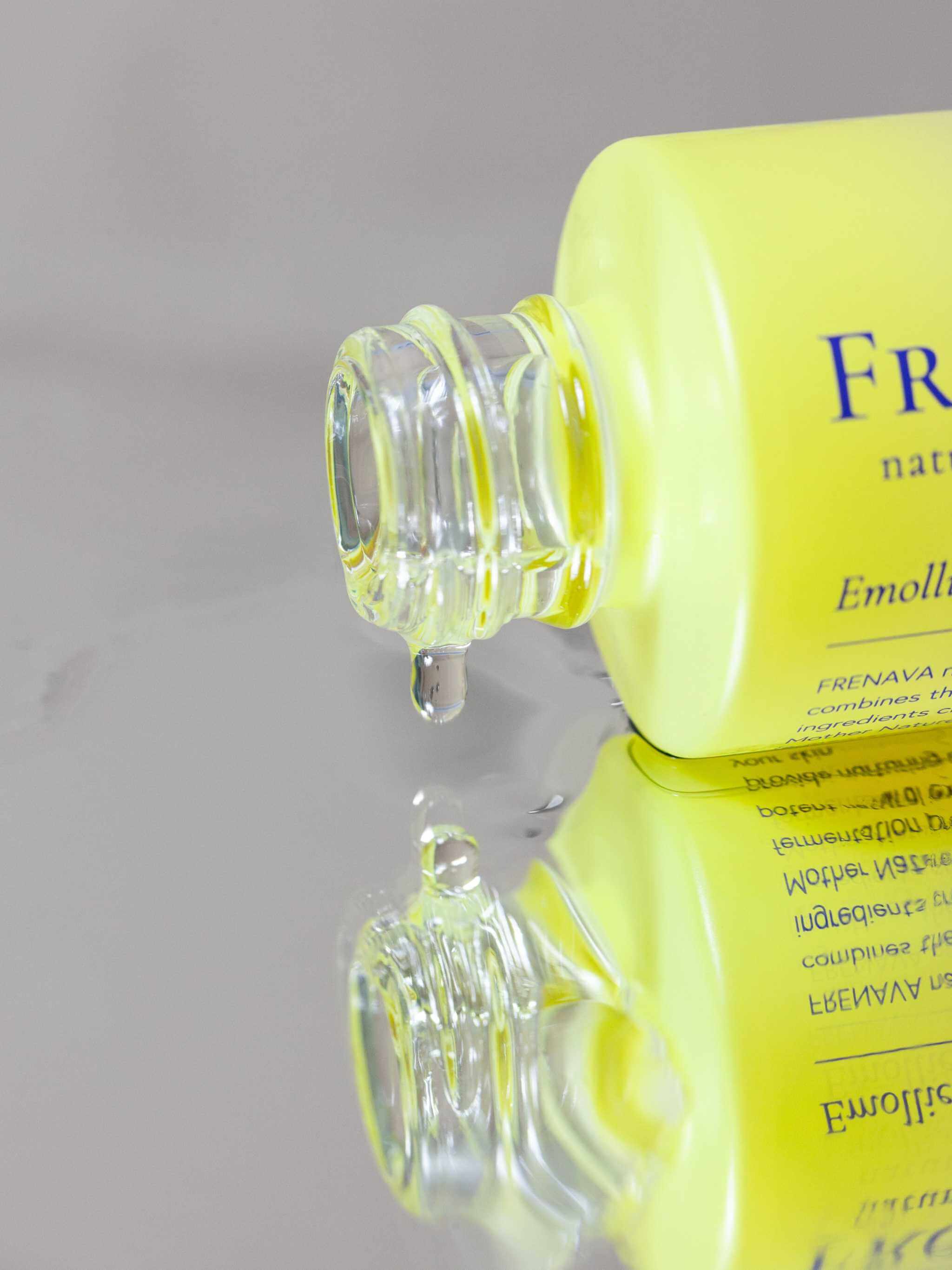 Frenava Emollient Oil bottle with oil dripping, reflecting on a metallic surface.