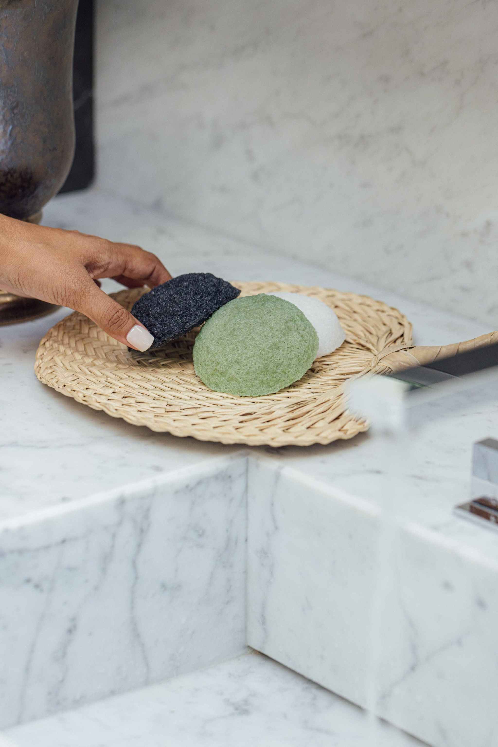 Shikohin Plant-Based Konjac Sponge in white, green, and black on a wicker tray near a sink.