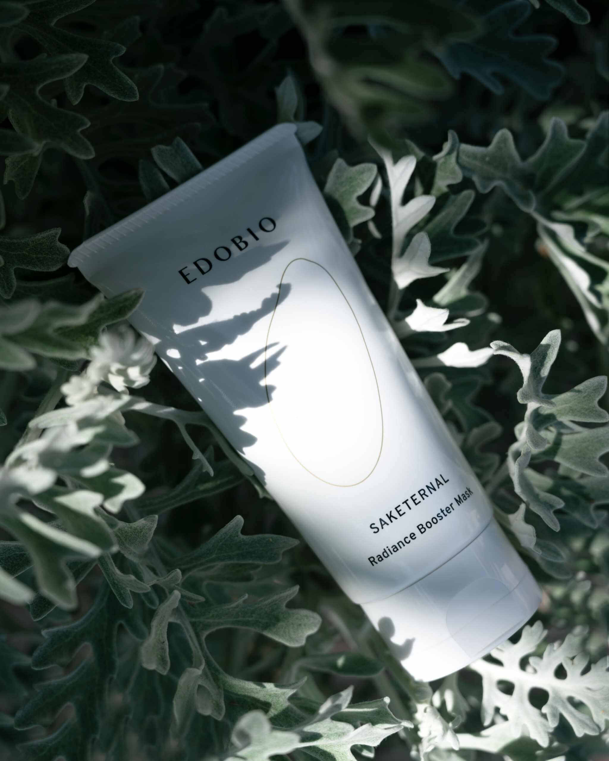 Edobio Radiance Booster Clay Face Mask amidst green foliage.