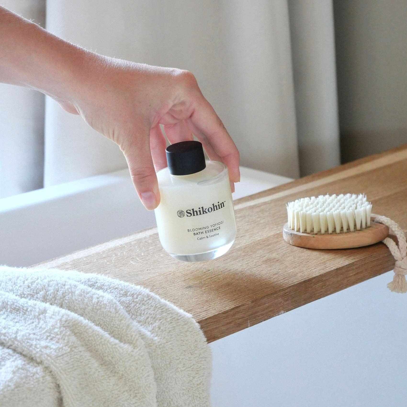 Blooming Yomogi Bath Soak Essence bottle near bath with towel and brush.