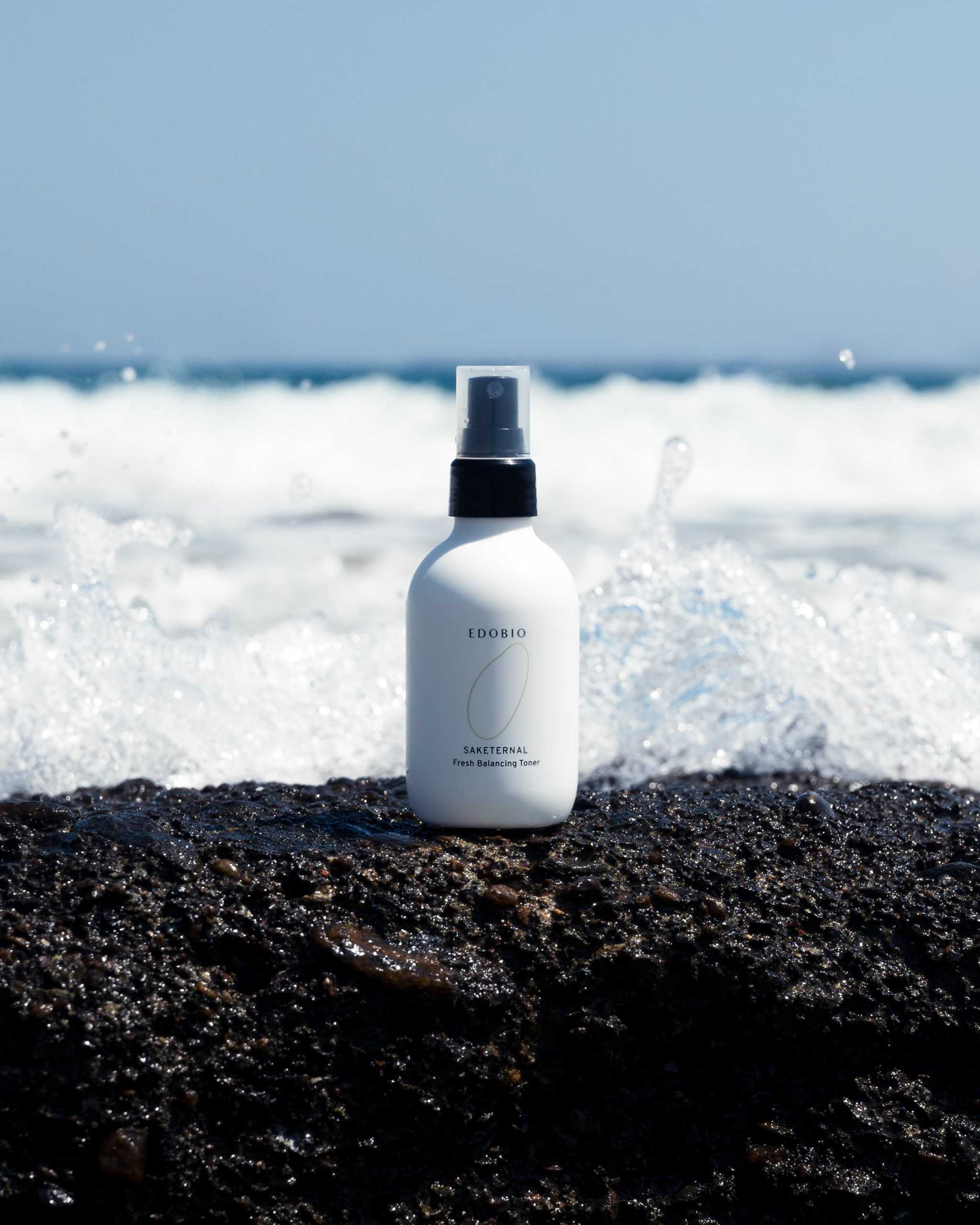 Edobio Fresh Balancing Toner bottle on a rocky shoreline with ocean waves in the background.